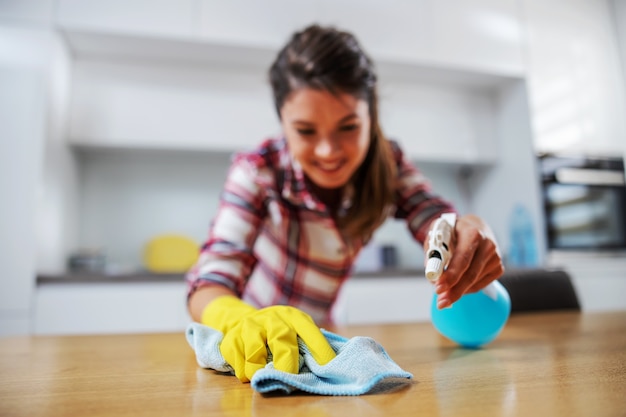 Casalinga diligente che strofina il tavolo della cucina con il detersivo.