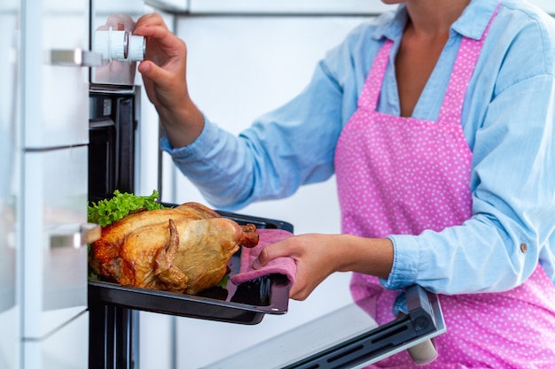 Casalinga in grembiule che cuoce pollo con le verdure nel forno per la cena a casa. Anatra da forno per le vacanze