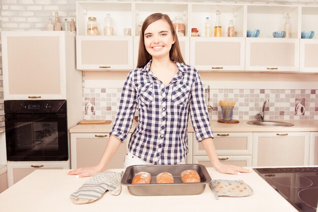 Casalinga sorridente abbastanza giovane in cucina con pane cotto