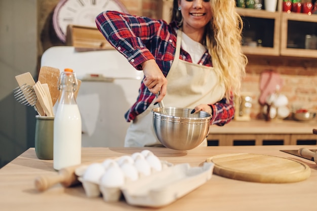 Casalinga sorridente in grembiule che produce pasta nella ciotola