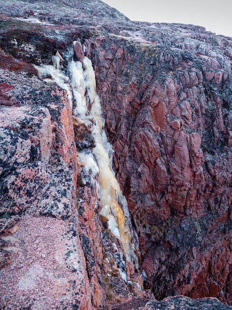 Cascata ghiacciata da una scogliera. Atmosferico paesaggio artico minimalista con un ghiacciaio sospeso sulla cima di una montagna rocciosa. Penisola di Kola.