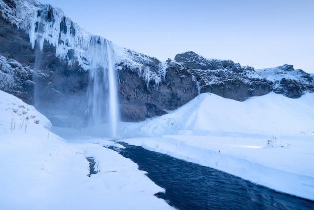Cascata Seljalandsfoss Islanda Paesaggio invernale islandese Alta cascata e rocce Neve e ghiaccio Potente flusso d'acqua dalla scogliera Un luogo popolare per viaggiare in Islanda