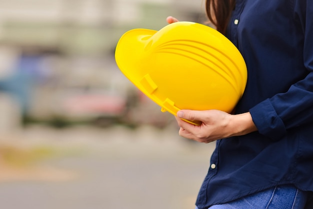 Casco giallo del casco della tenuta della costruzione di edifici di ingegneria delle donne che sta nel luogo di lavoro