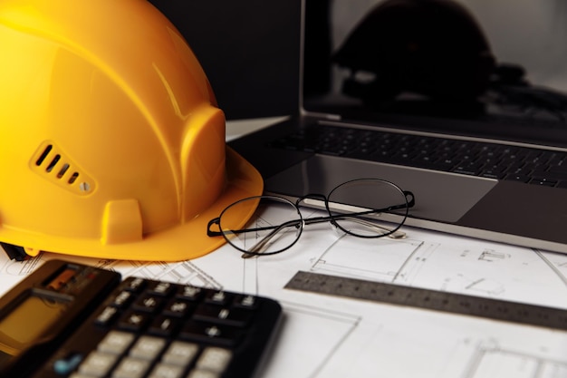 Casco giallo, occhiali e laptop sui piani di costruzione.