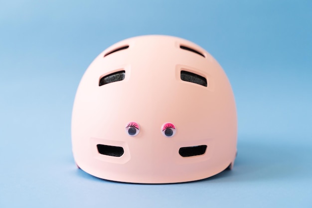 Casco rosa con divertenti occhi di bambola su sfondo blu Protezione per la sicurezza delle attività all'aperto dei bambini