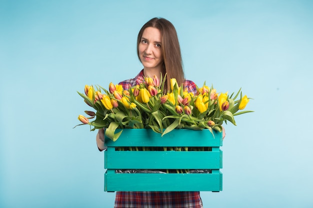 Casella di tenuta caucasica felice della giovane donna con i tulipani sulla superficie blu
