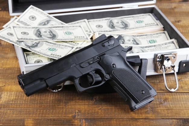 Caso con denaro e pistola su sfondo di legno