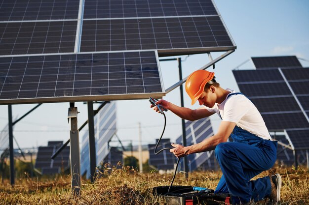 Caso di apertura con attrezzatura. Lavoratore maschio in uniforme blu all'aperto con batterie solari al giorno pieno di sole.