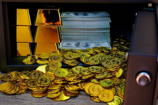 Cassaforte in acciaio piena di pila di monete e lingotto d'oro e banconota da 100 USD sul tavolo di legno