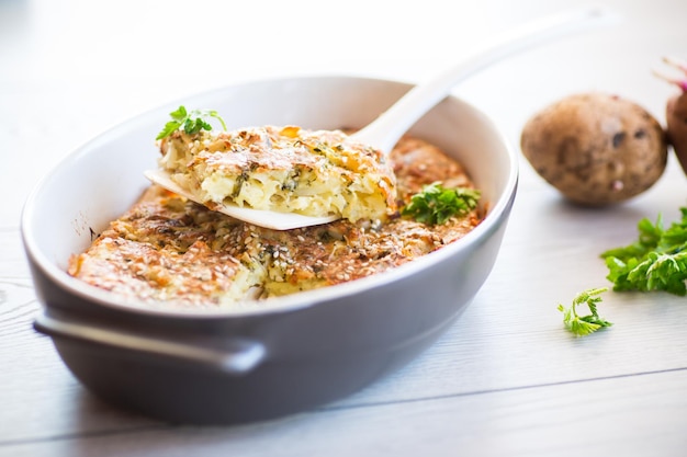 casseruola di patate con cavolo e spezie in forma ceramica su un tavolo di legno