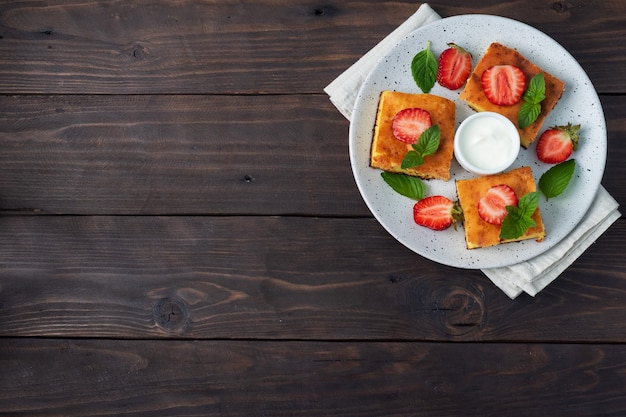 Casseruola di ricotta con fragole e menta. Delizioso dessert fatto in casa a base di cagliata e frutti di bosco freschi con panna. sfondo in legno scuro, copia spazio.