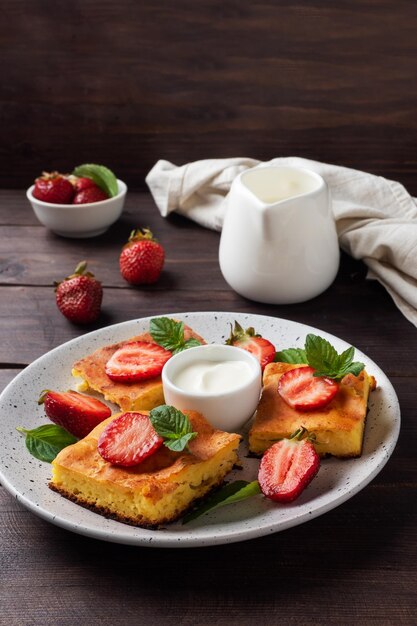 Casseruola di ricotta con fragole e menta. Delizioso dessert fatto in casa a base di cagliata e frutti di bosco freschi con panna. sfondo in legno scuro, copia spazio.