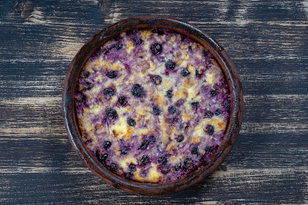 Casseruola dolce della ricotta con ribes nero e semola sulla tavola di legno. Ciotola in ceramica con casseruola di ricotta al forno, primo piano