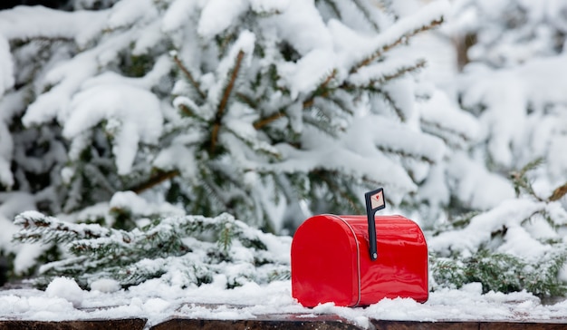 Cassetta postale rossa sulla tavola di legno nella neve