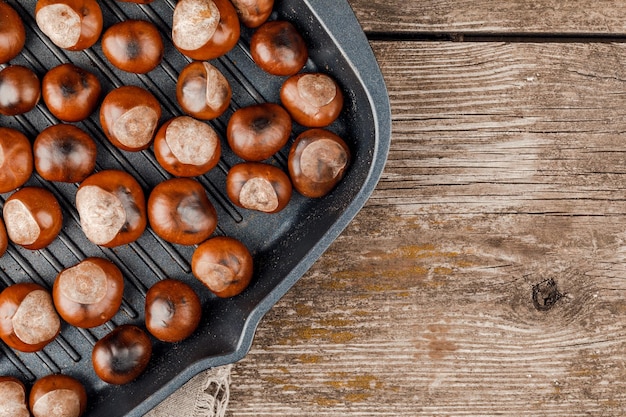 Castagne arrostite servite in un apposito tegame forato di castagne su un tavolo di legno.