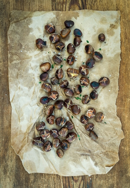 Castagne arrostite su carta artigianale oleosa consumata su legno rustico, vista dall'alto.