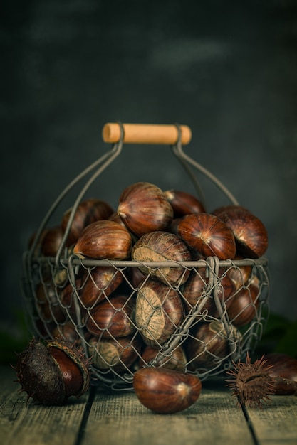 Castagne crude su un legno in un cesto di ferro.