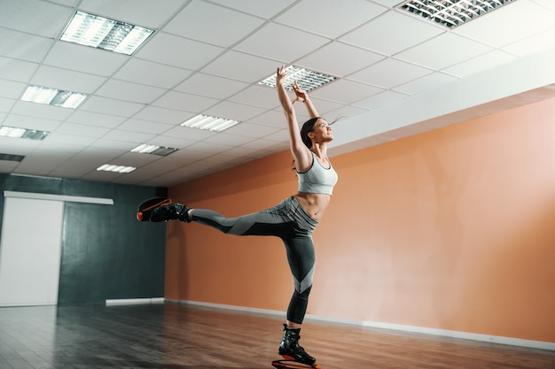 Castana caucasica di bella misura in abiti sportivi che saltano sulle calzature di salti di kangoo in palestra.