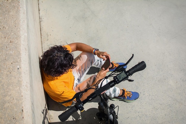 Casual Donna Seduta Sull'asfalto Usando Il Suo Smartphone Accanto A Uno Scooter Elettrico.