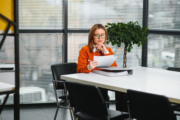 Casual imprenditrice in maglione seduto alla sua scrivania in ufficio