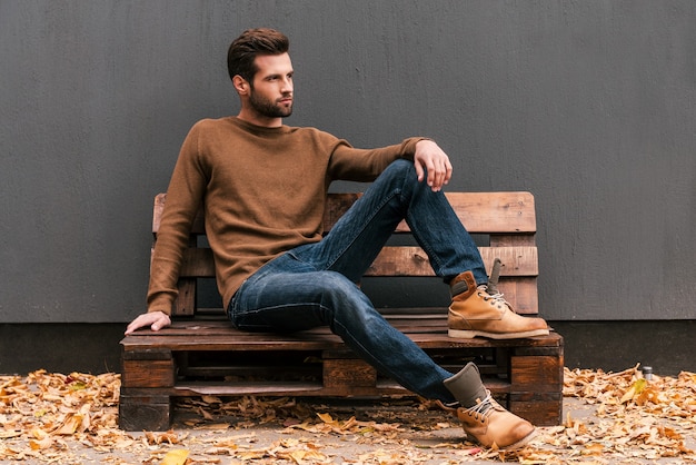 Casualmente bello. Bel giovane seduto sul pallet di legno e guardando lontano