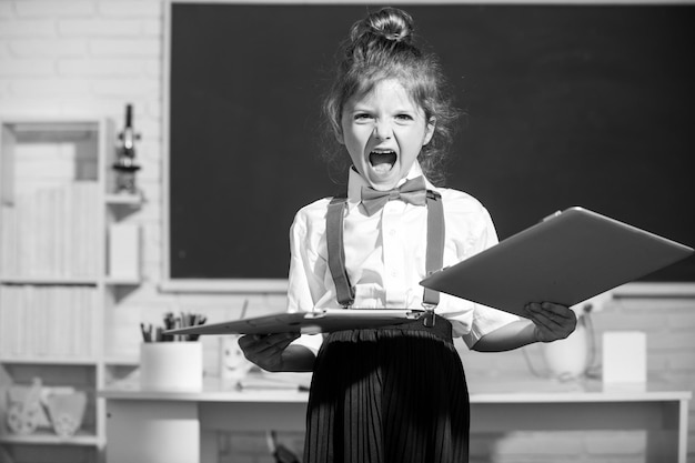 Cattiva ragazza della scuola arrabbiata contro istruzione a distanza. Bambino triste rotto il laptop online a scuola. Distruggendo la tecnologia informatica danneggiata. Problema dei bambini con l'apprendimento a distanza.