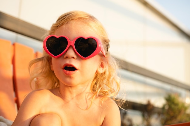 Caucasica bambina bambino bambino indossando ping cuore forma occhiali da sole sorpreso primo piano stile di vita all'aperto