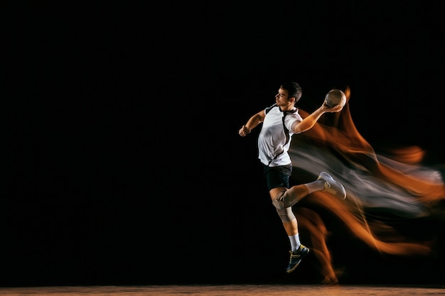 Caucasico giovane giocatore di pallamano in azione e movimento in luci miste su sfondo nero studio. Sportivo professionista maschio in forma. Concetto di sport, movimento, energia, stile di vita dinamico e sano.