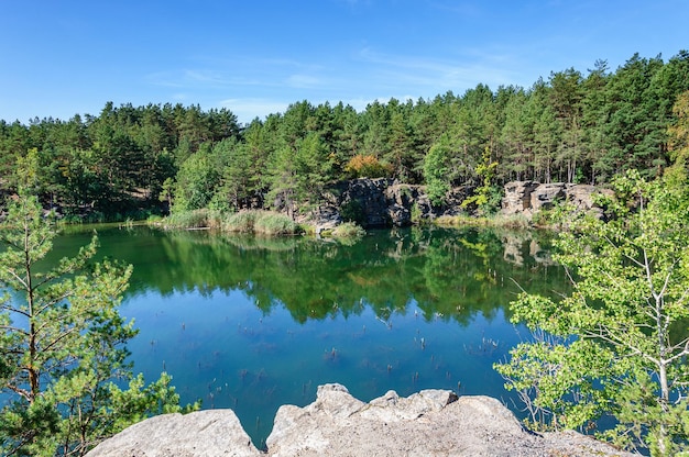 Cava di granito allagata con alberi di pino sulla riva e cielo blu, Korostyshiv, Ucraina