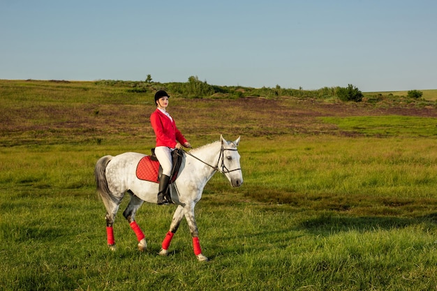 Cavaliere di giovane donna, indossa redingote rossa e calzoni bianchi, con il suo cavallo alla luce del tramonto serale. Fotografia all'aperto in uno stile di vita