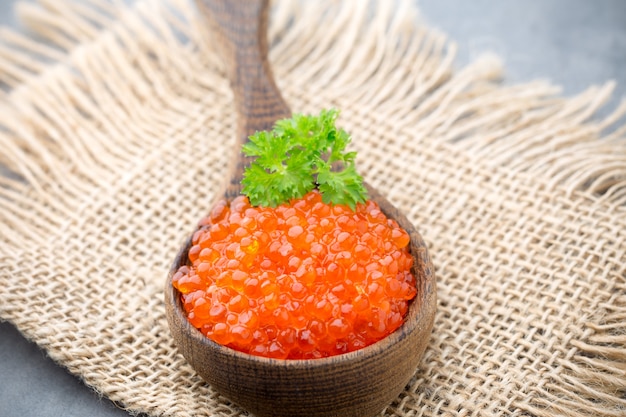 Caviale di salmone con cucchiaio su sfondo grigio.