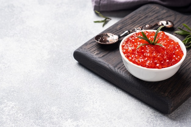 Caviale di salmone rosso in un piatto su un tagliere di legno. Calcestruzzo grigio con copia spazio. Prelibatezza di snack.