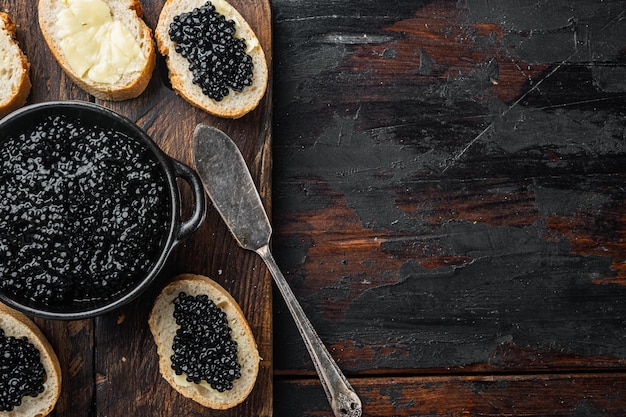 Caviale nero servito su baguette, su un vecchio sfondo di tavolo in legno scuro, vista dall'alto piatta con spazio di copia per il testo