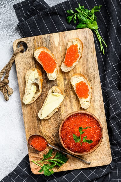 Caviale rosso in ciotola di legno e panini sul tagliere.