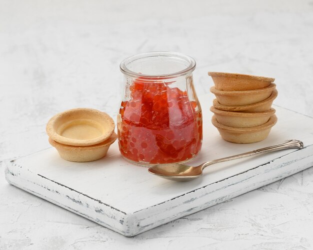 caviale rosso in un barattolo di vetro e tortelle rotonde su un tavolo bianco