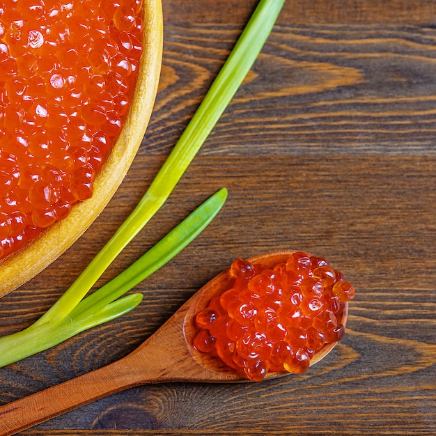 Caviale rosso in una tazza di legno su una parete di legno con un cucchiaio.