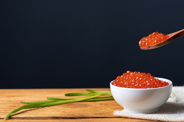 Caviale rosso in una tazza di legno su uno sfondo di legno con un cucchiaio. Posto per pubblicità, logo, etichetta, mockup, mock-up.