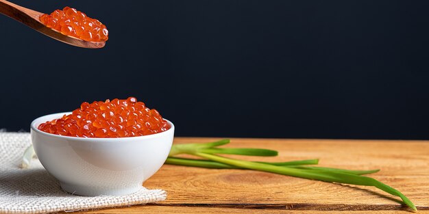 Caviale rosso in una tazza di legno su uno sfondo di legno con un cucchiaio.