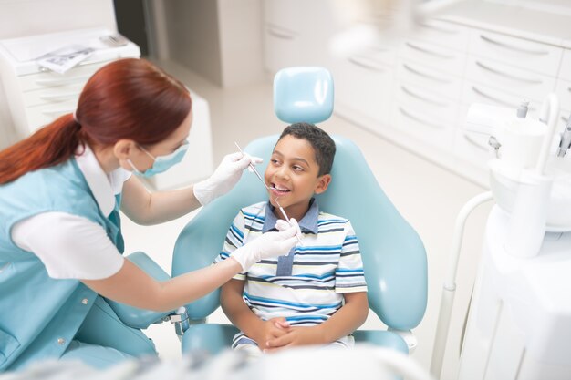 Cavità d'esame del dentista. Bel ragazzo carino dagli occhi scuri che apre la bocca mentre il dentista esamina la cavità