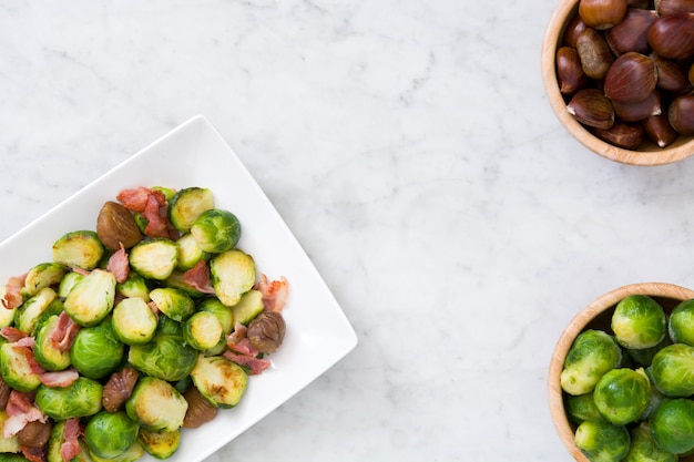 Cavoletti di Bruxelles con le castagne e la pancetta affumicata sulla vista superiore di marmo bianca