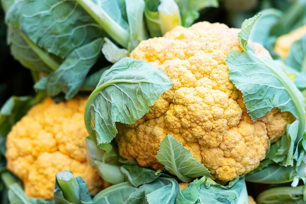 Cavolfiore giallo con foglie sullo sfondo vegetale del mercato