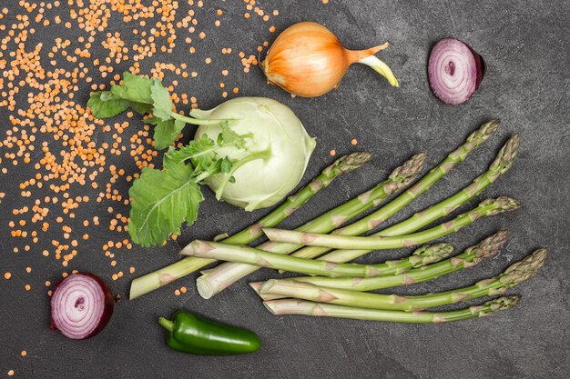 Cavolo rapa e asparagi verdi sul tavolo. Cipolle e lenticchie. Sfondo nero. Lay piatto