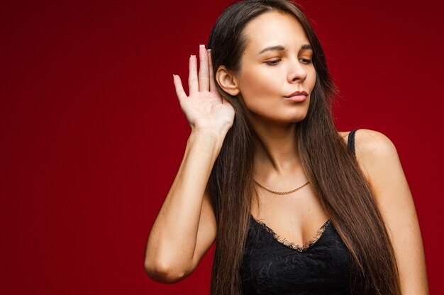 Ccaucasian donna con aspetto attraente ascolta qualcuno, immagine isolata sulla parete rossa