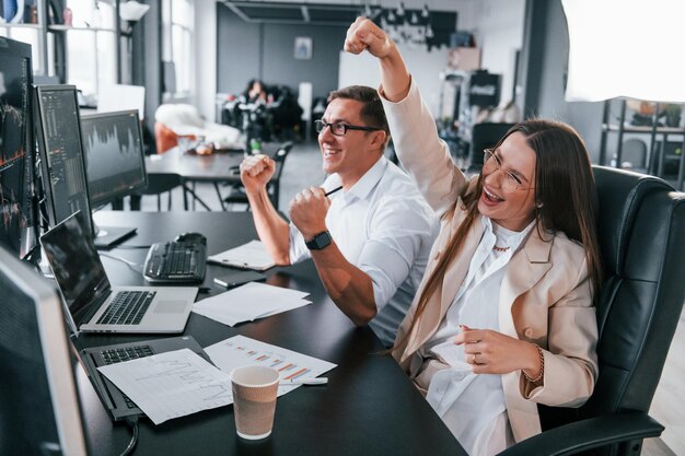 Celebra il successo Il team di agenti di cambio lavora in un ufficio moderno con molti schermi