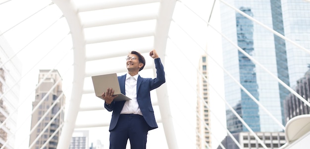 Celebrando il successo a braccia alzate. Uomo d'affari asiatico allegro che celebra il successo all'aperto