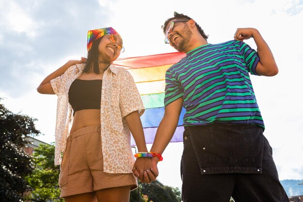 Celebrando la diversità delle coppie che si tengono per mano con la bandiera arcobaleno nel parco guardandosi l'un l'altro