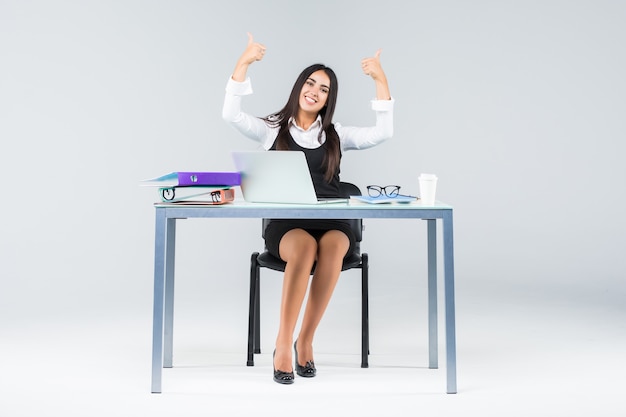 Celebrando la donna di affari che si siede sul tavolo con il computer portatile isolato su bianco