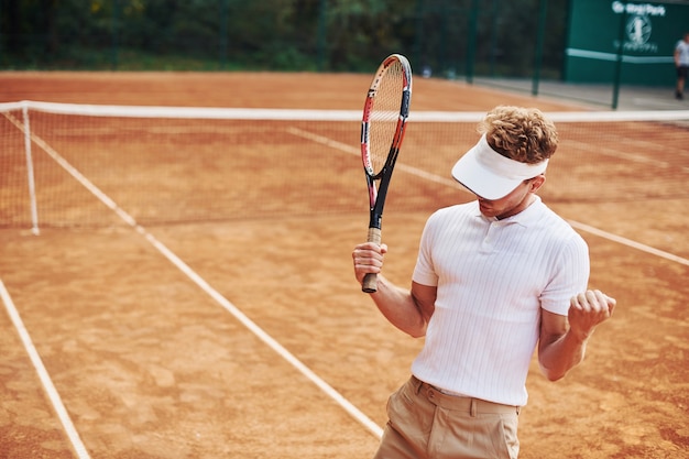 Celebrando la vittoria. Il giovane tennista in abiti sportivi è in campo all'aperto.