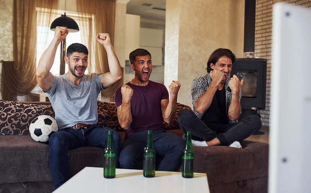 Celebrando la vittoria. Tre amici eccitati che guardano insieme il calcio in TV a casa.