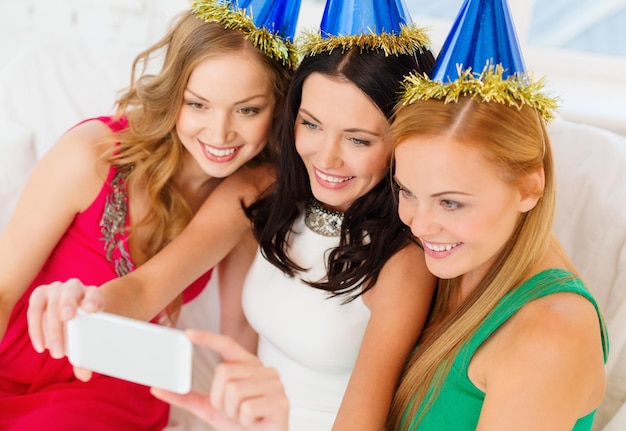 celebrazione, amici, addio al nubilato, concetto di compleanno - tre donne sorridenti con cappelli blu che si divertono con la fotocamera dello smartphone